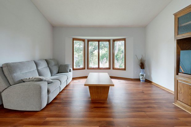 Spacious living room with wooden floors, gray sofa, and large bay windows.
